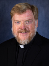 A person with a beard and a priest's collar

Description automatically generated