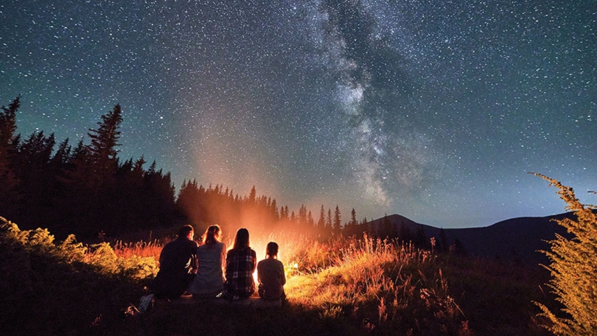 family sitting around a campfire under a starry night sky