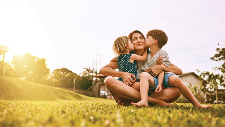mom sitting on grass and hugging her two kids 